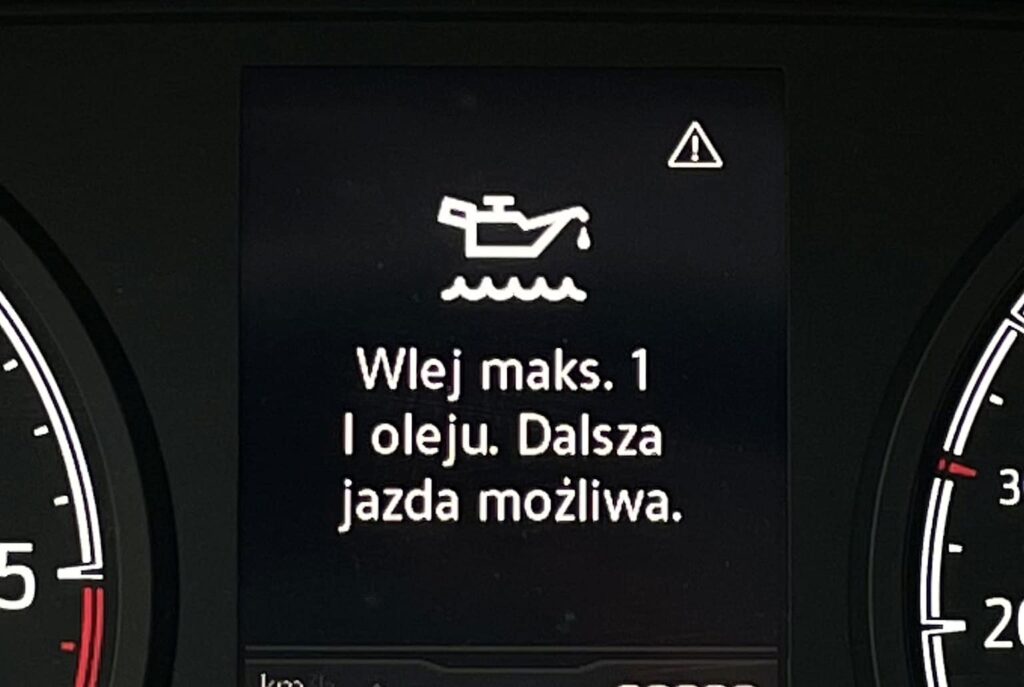 Kontrolka oleju na desce rozdzielczej samochodu wskazująca konieczność dolania do 1 litra oleju, z komunikatem informującym, że dalsza jazda jest możliwa.